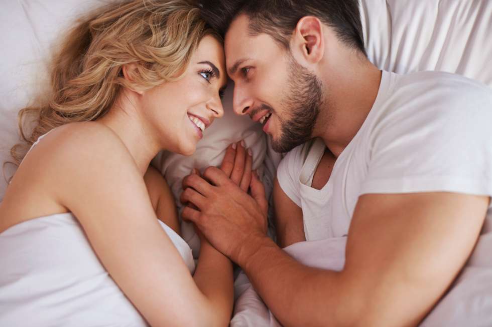 Casal sorrindo na cama | Sexo para tratamento do cálculo renal